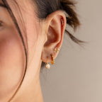 Close-up of a woman's ear with multiple gold and crystal earrings, featuring the Chandelier Diamond Huggies in art deco style.