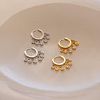 Two pairs of Chandelier Diamond Huggies, featuring an elegant hoop design in silver and gold, are displayed on a smooth, light-colored surface.