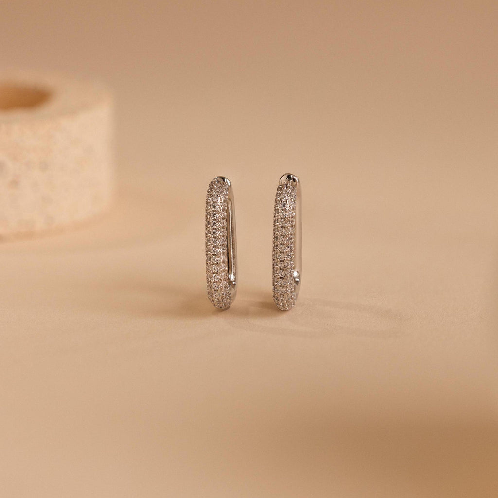 Chunky Pave Link Earrings featuring geometric hoops adorned with small sparkling stones, shown on a beige surface.