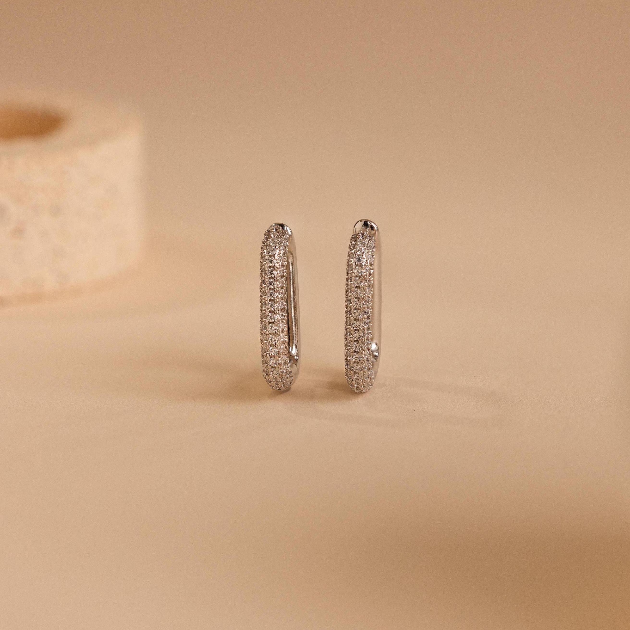 Chunky Pave Link Earrings featuring geometric hoops adorned with small sparkling stones, shown on a beige surface.
