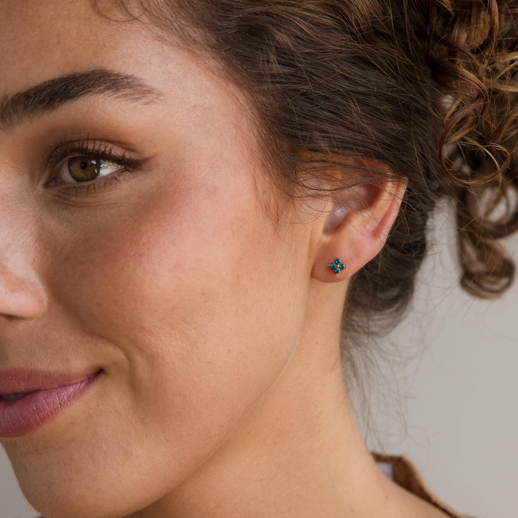 Close-up of a woman smiling, wearing Ivy Flower Birthstone Studs in her pierced ear. The turquoise sterling silver earring stands out against her curly hair on the right.