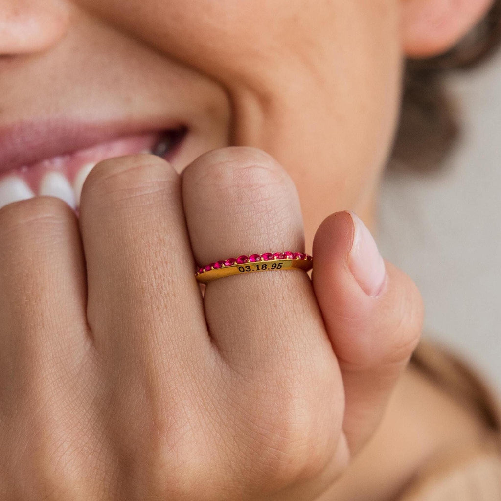 A person smiles while wearing the Engraved Birthstone Eternity Ring, a gold personalized ring with red stones and the engraved date 03.18.96, highlighting its unique and meaningful design.