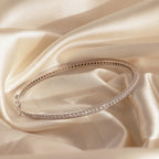 A Diamond Tennis Bangle with a curved design is shown on soft, cream satin fabric.