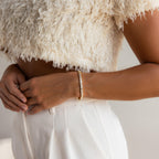 Woman wearing a textured cream crop top, white pants, and the Vertical Baguette Tennis Bracelet in gold with baguette diamonds, her hand resting on her hip.