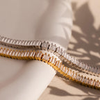 The Vertical Baguette Tennis Bracelet, available in gold and silver tones, features elegant rectangular-cut stones that capture the timeless glamour of Art Deco style, shown against a neutral background.