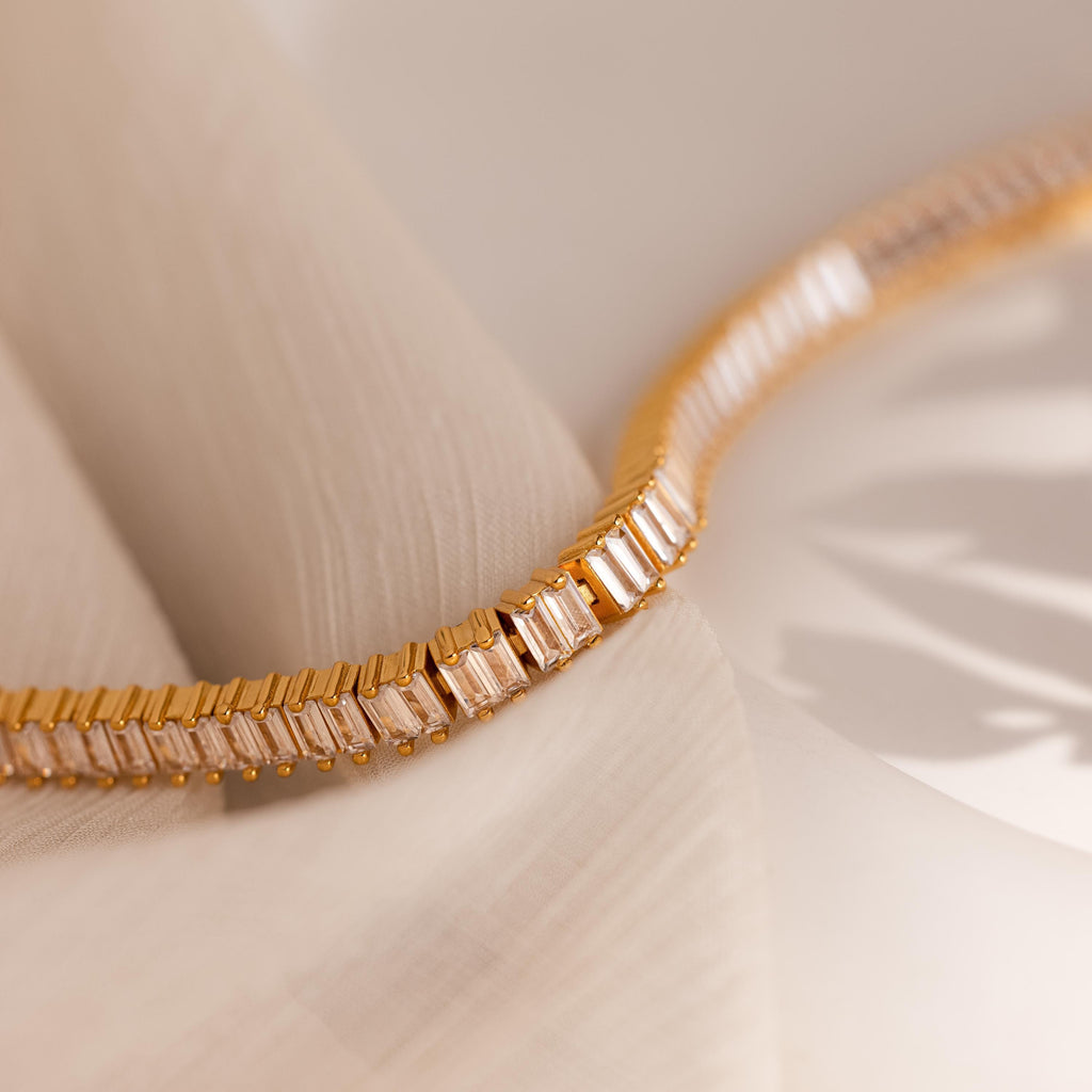 The Vertical Baguette Tennis Bracelet, featuring rectangular gemstones in an Art Deco style, is displayed on soft, light fabric under gentle lighting.