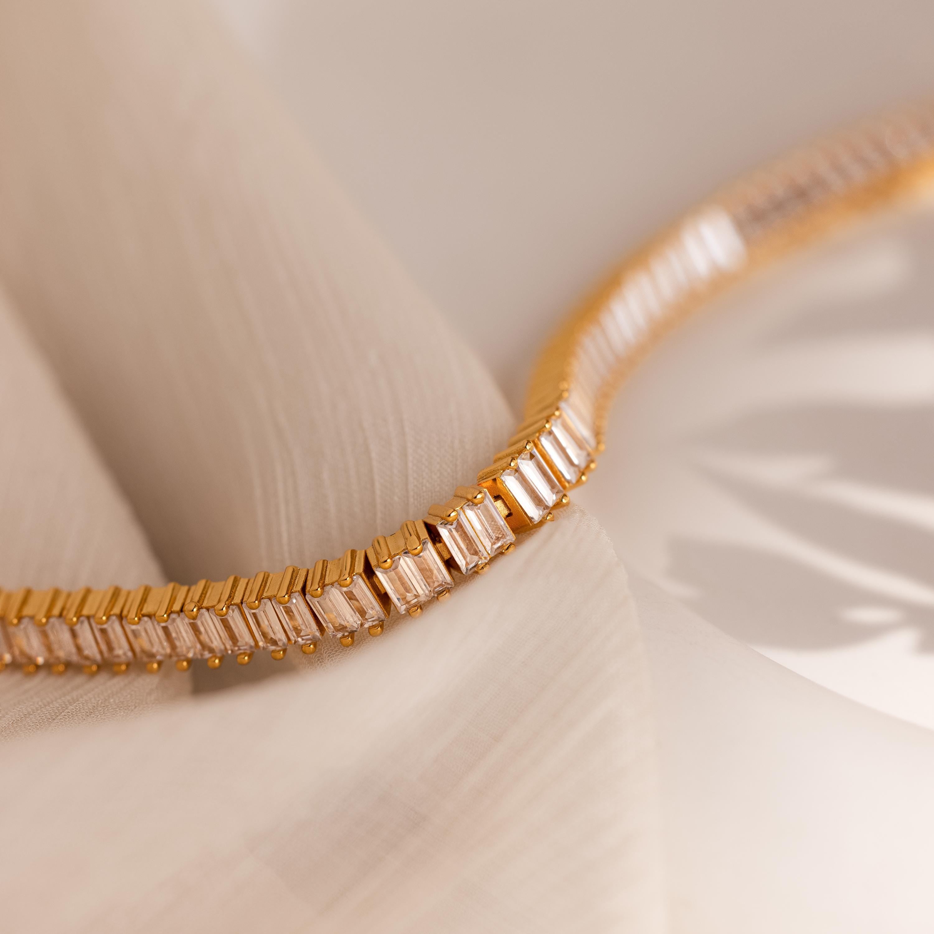 The Vertical Baguette Tennis Bracelet, featuring rectangular gemstones in an Art Deco style, is displayed on soft, light fabric under gentle lighting.