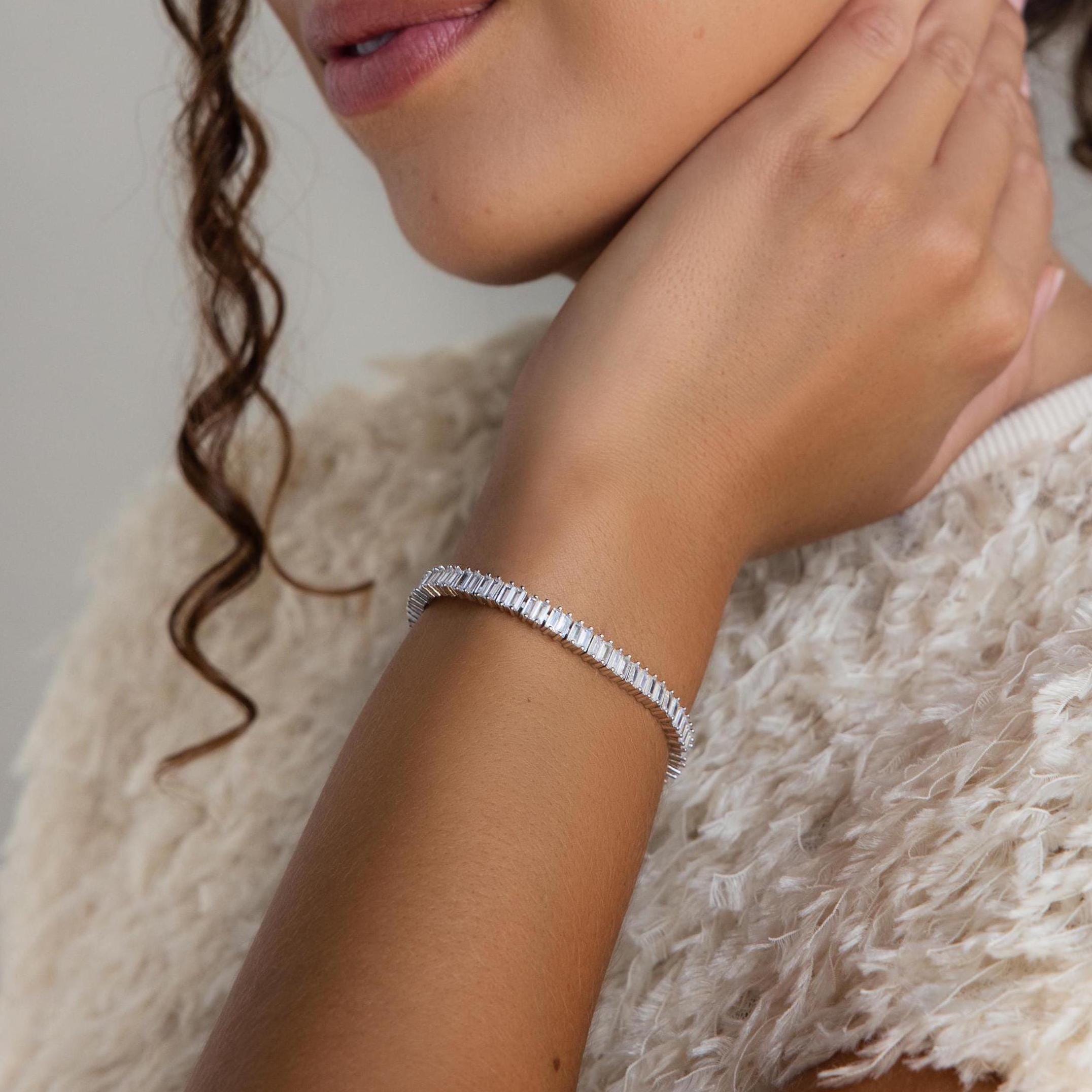 A woman in a textured cream top touches her neck, wearing the Vertical Baguette Tennis Bracelet.