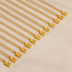 The Ribbed Birthstone Star Necklaces are displayed diagonally on beige, each gold necklace featuring a rectangular pendant with a unique colored gemstone—ideal for starting or gifting a birthstone necklace collection.