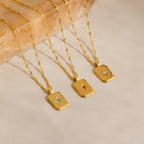 The Ribbed Birthstone Star Necklace, a gold necklace with a rectangular pendant featuring a unique gemstone, is displayed on stone. Its ribbed design and personalized birthstone make it both stylish and meaningful.