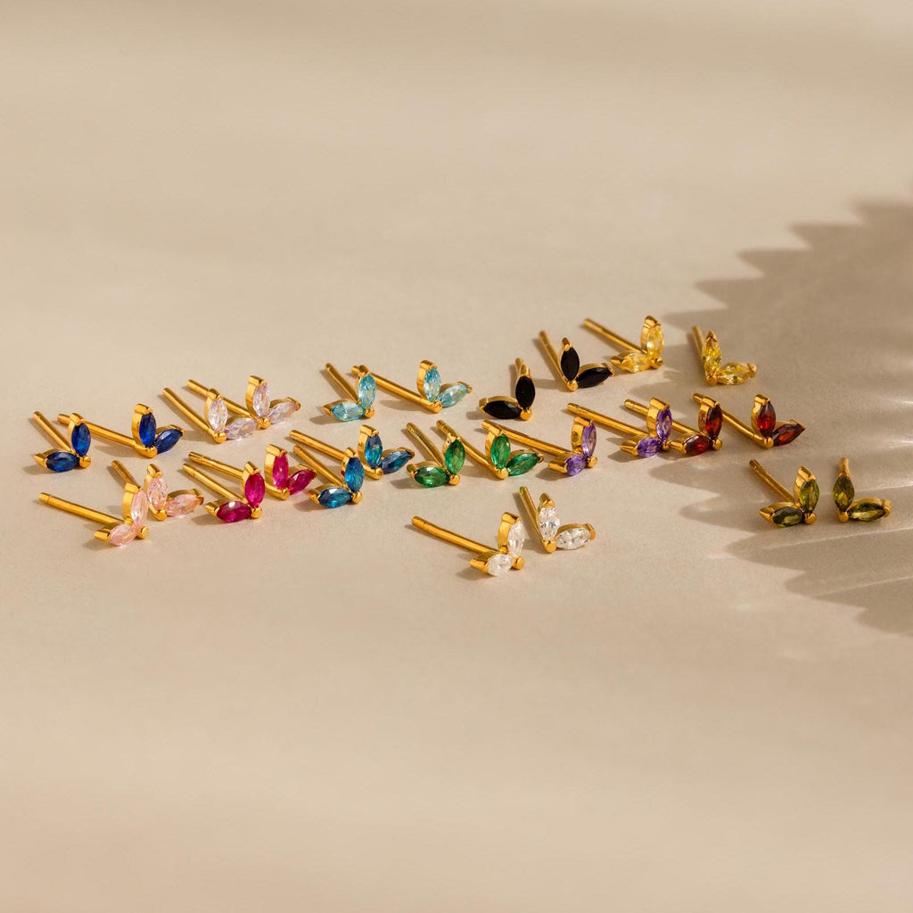 The Marquise Petal Birthstone Studs, gold earrings with colorful gemstones, are arranged neatly on a neutral surface with patterned shadows—ideal for lovers of personalized jewelry.