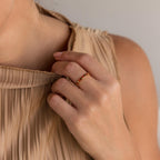 A woman in a pleated beige top holds the collar, displaying the Half Eternity Birthstone Ring with red stones—a stylish anniversary keepsake on her finger.