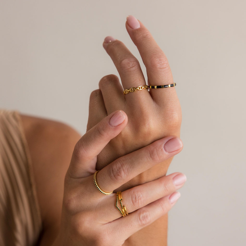 Hands with manicured nails wear the Half Eternity Birthstone Ring, featuring gold and black baguette-cut gemstones, posed against a neutral background.