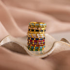Stack of colorful gemstone rings, including the Half Eternity Birthstone Ring, displayed on a wavy ceramic dish with a soft beige fabric background.