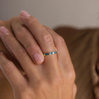 A hand with neatly manicured nails wears the Half Eternity Birthstone Ring, featuring thin gold and blue square-shaped baguette-cut stones—a stunning choice for an anniversary keepsake.