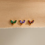 Three pairs of Marquise Petal Birthstone Studs—ideal as birthstone earrings or personalized jewelry—sparkle in green, purple, and red tones on a beige fabric background.