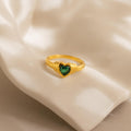 The Birthstone Heart Signet Ring showcases a green heart-shaped gemstone, beautifully presented on cream-colored fabric.