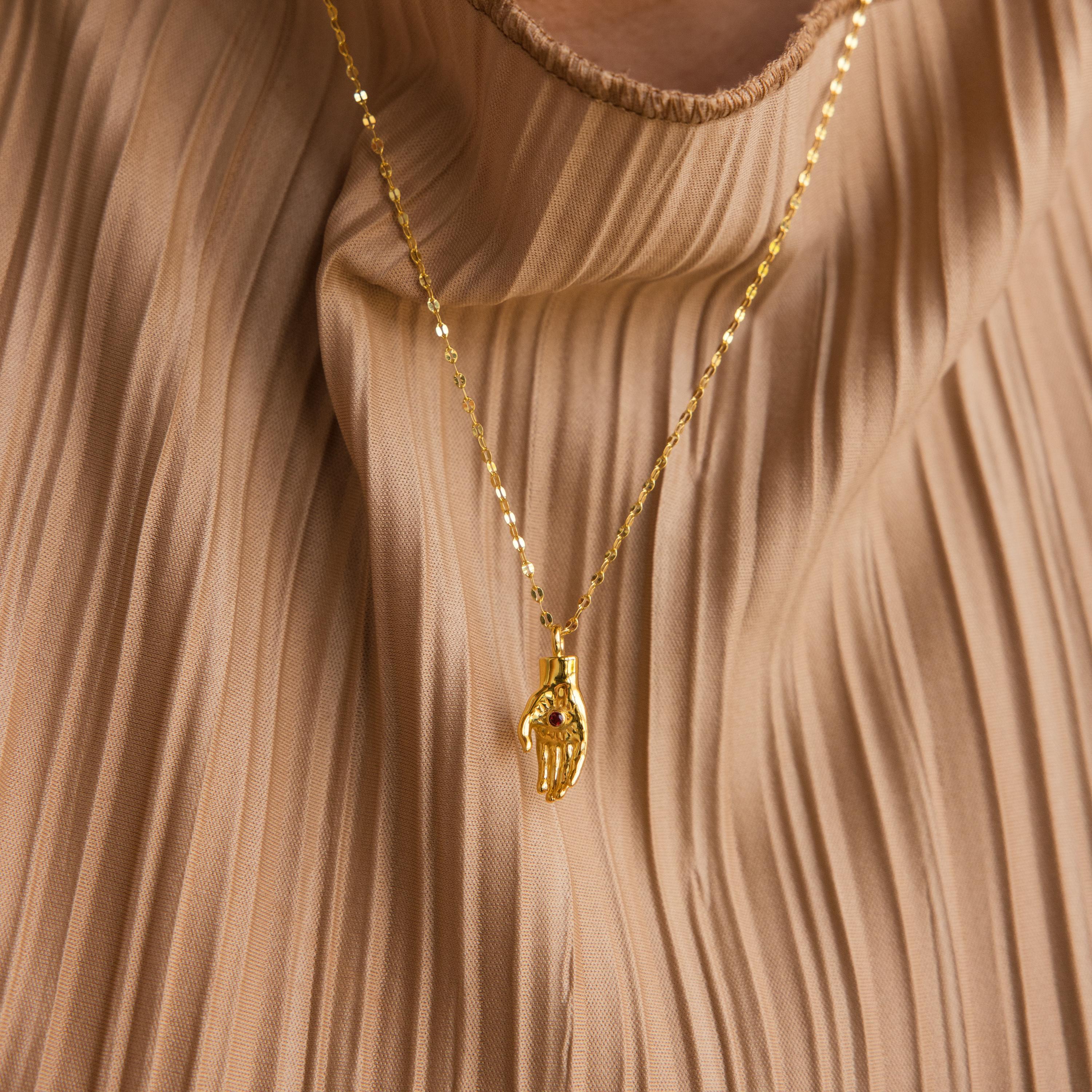 Evil Eye Birthstone Hand Necklace featuring a skeletal hand pendant, displayed on pleated beige fabric—blending edgy allure with the protective symbolism of the evil eye.