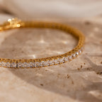 The Princess Diamond Tennis Bracelet is displayed on a textured beige stone surface, illuminated by soft lighting.