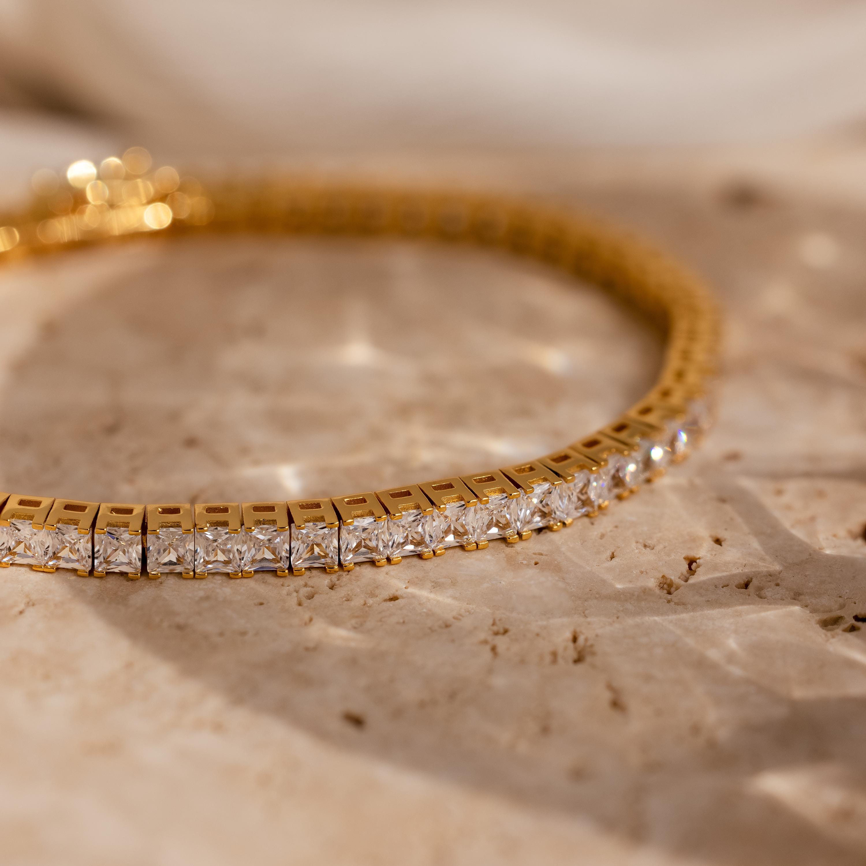 The Princess Diamond Tennis Bracelet is displayed on a textured beige stone surface, illuminated by soft lighting.