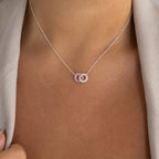 A close-up of the Interlocking Duo Birthstone Necklace, featuring two silver rings, stylishly paired with a light-colored blazer.