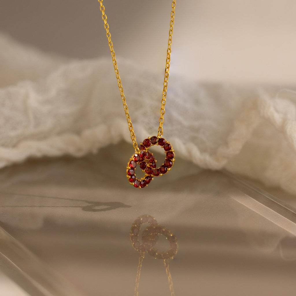 Interlocking Duo Birthstone Necklace with two red gemstone circles, beautifully showcased against soft white fabric.