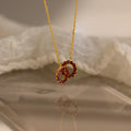 Interlocking Duo Birthstone Necklace with two red gemstone circles, beautifully showcased against soft white fabric.