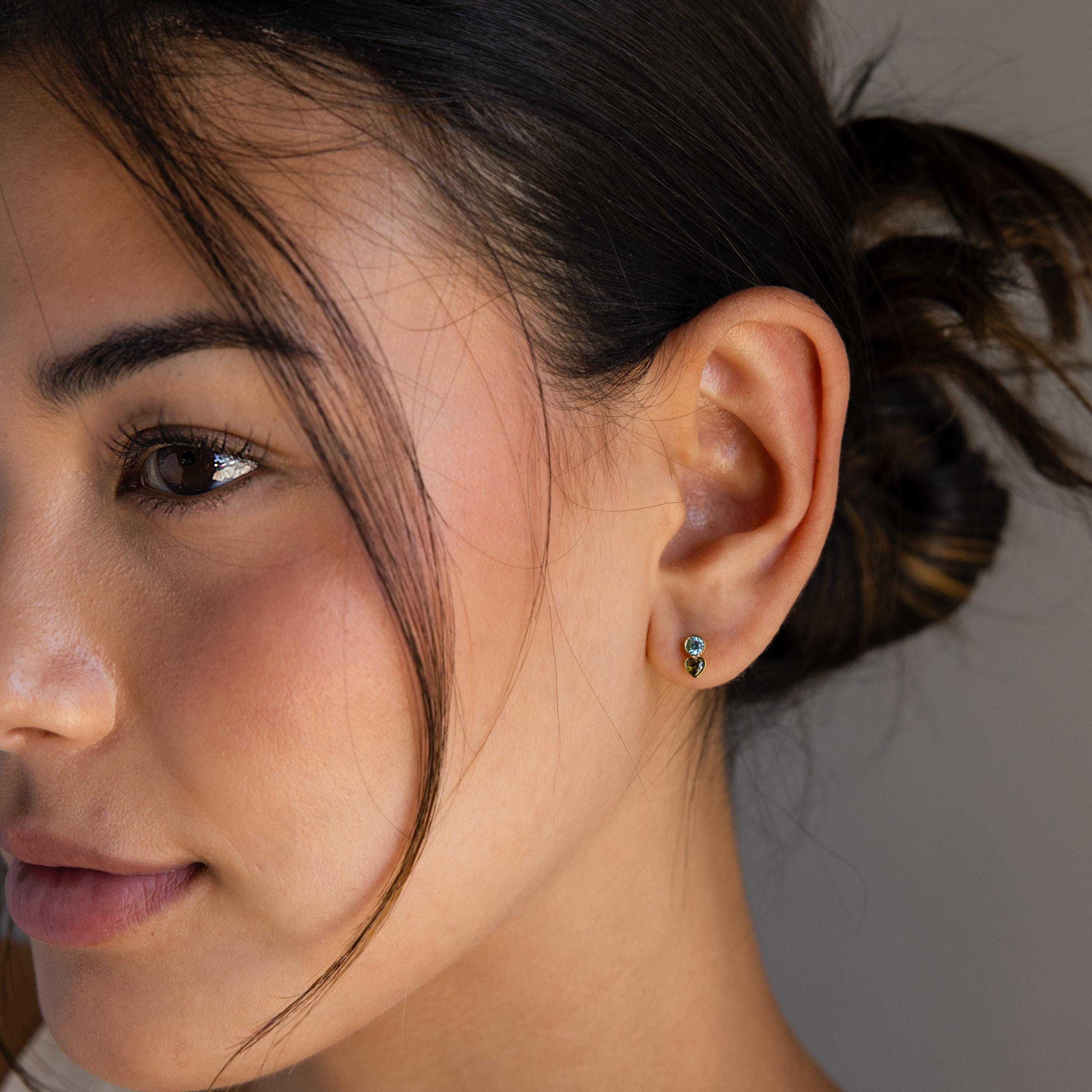 A close-up shows a woman’s ear adorned with Toi et Moi Birthstone Studs, her hair tied back in soft lighting—making these personalized stud earrings a perfect custom gift.