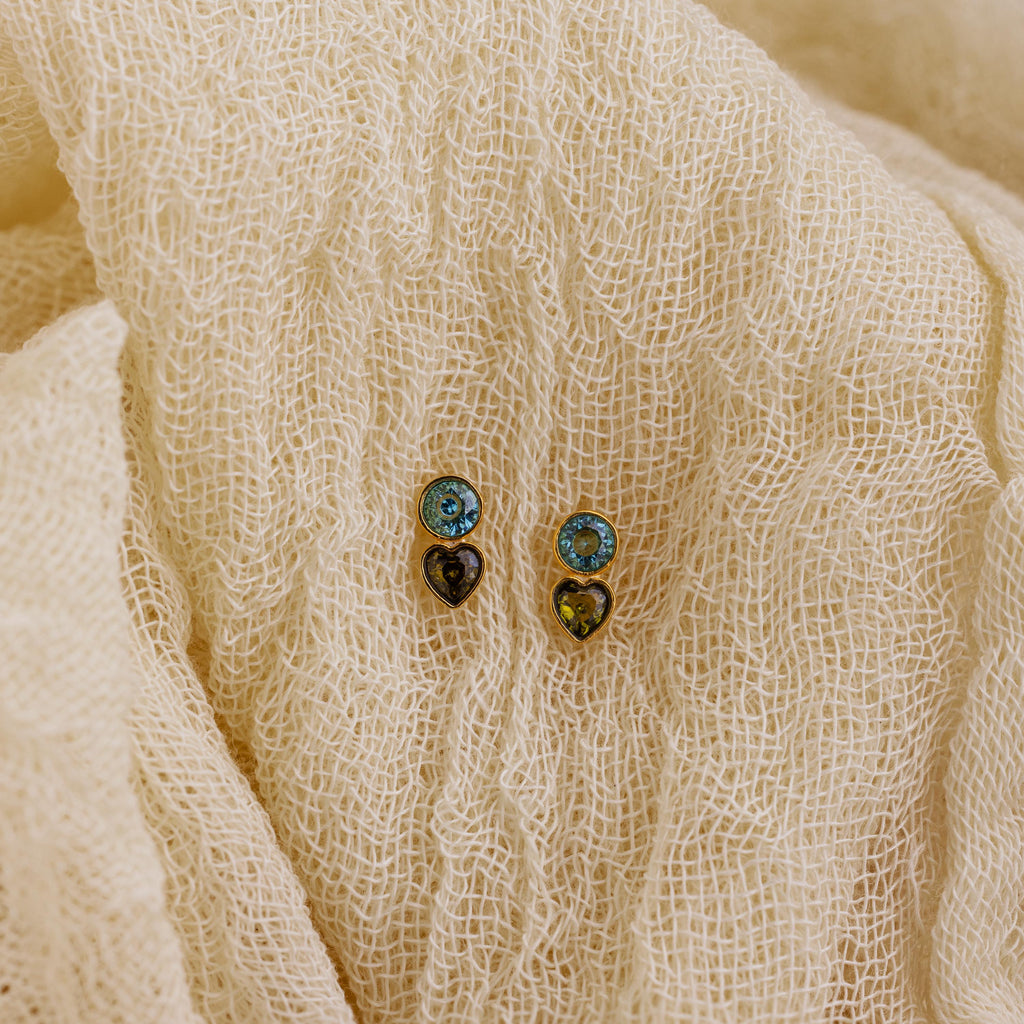 Two pairs of Toi et Moi Birthstone Studs in blue and gold rest on textured cream fabric—ideal as a custom gift or to add a personalized touch to your jewelry collection.