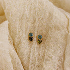 Two pairs of Toi et Moi Birthstone Studs in blue and gold rest on textured cream fabric—ideal as a custom gift or to add a personalized touch to your jewelry collection.