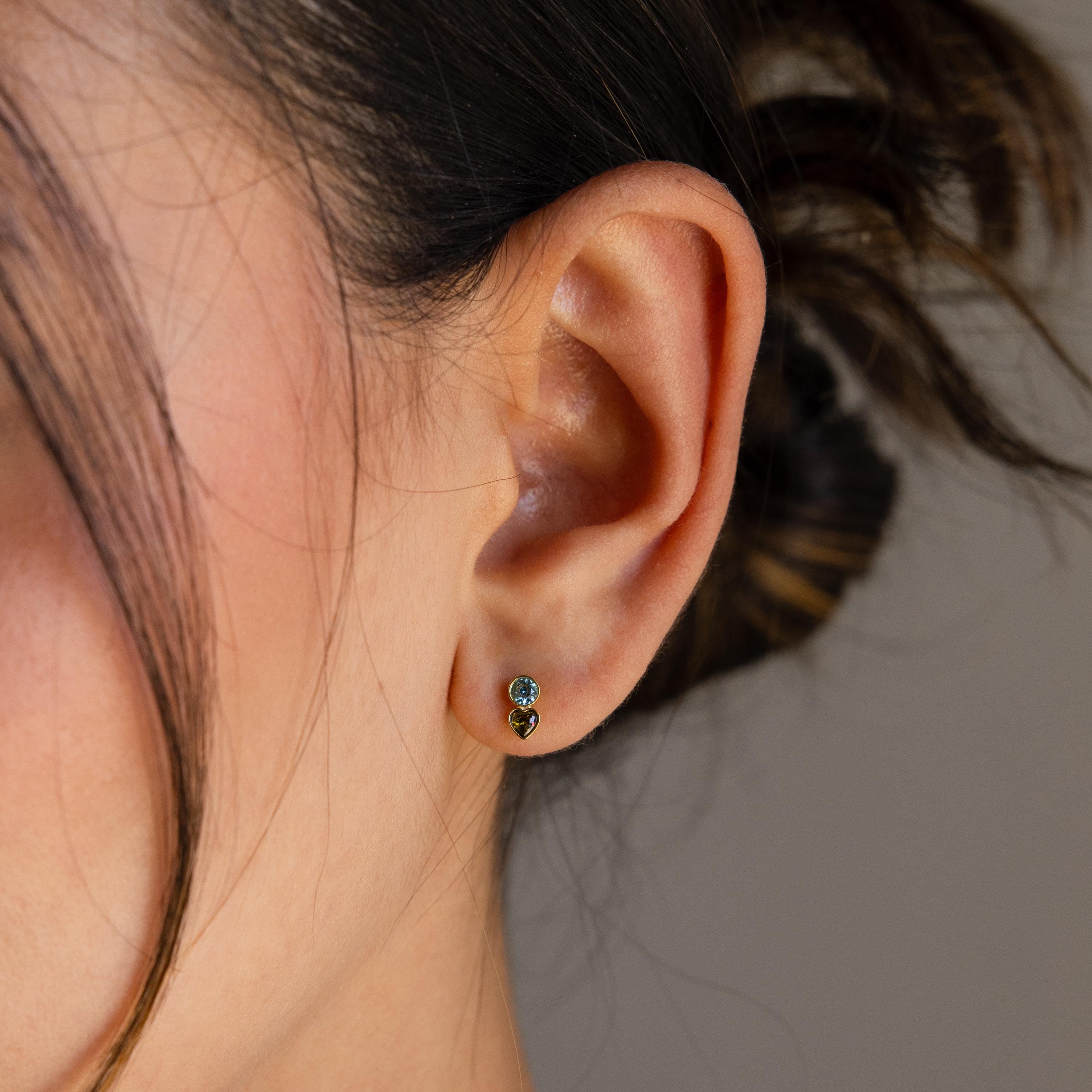 Close-up of a woman’s ear wearing Toi et Moi Birthstone Studs with two small gemstones; her hair is tied back, making these earrings an ideal personalized gift.