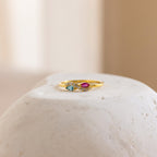Infinity Marquise Birthstone Ring, featuring blue and pink gemstones, is elegantly displayed on a smooth white stone with a soft, neutral background.