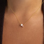 The Pearl & Birthstone Necklace is a personalized gold jewelry piece featuring a delicate pink birthstone pendant and elegant pearl accents, designed to rest gracefully on her neck.