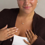 A woman with perfectly manicured nails wears a brown cardigan and showcases personalized jewelry, including rings, earrings, and the Pearl & Birthstone Necklace.