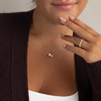 A woman wears the Pearl & Birthstone Necklace, a gold ring, brown cardigan, and white top—an elegant showcase of personalized jewelry that’s perfect for any occasion.