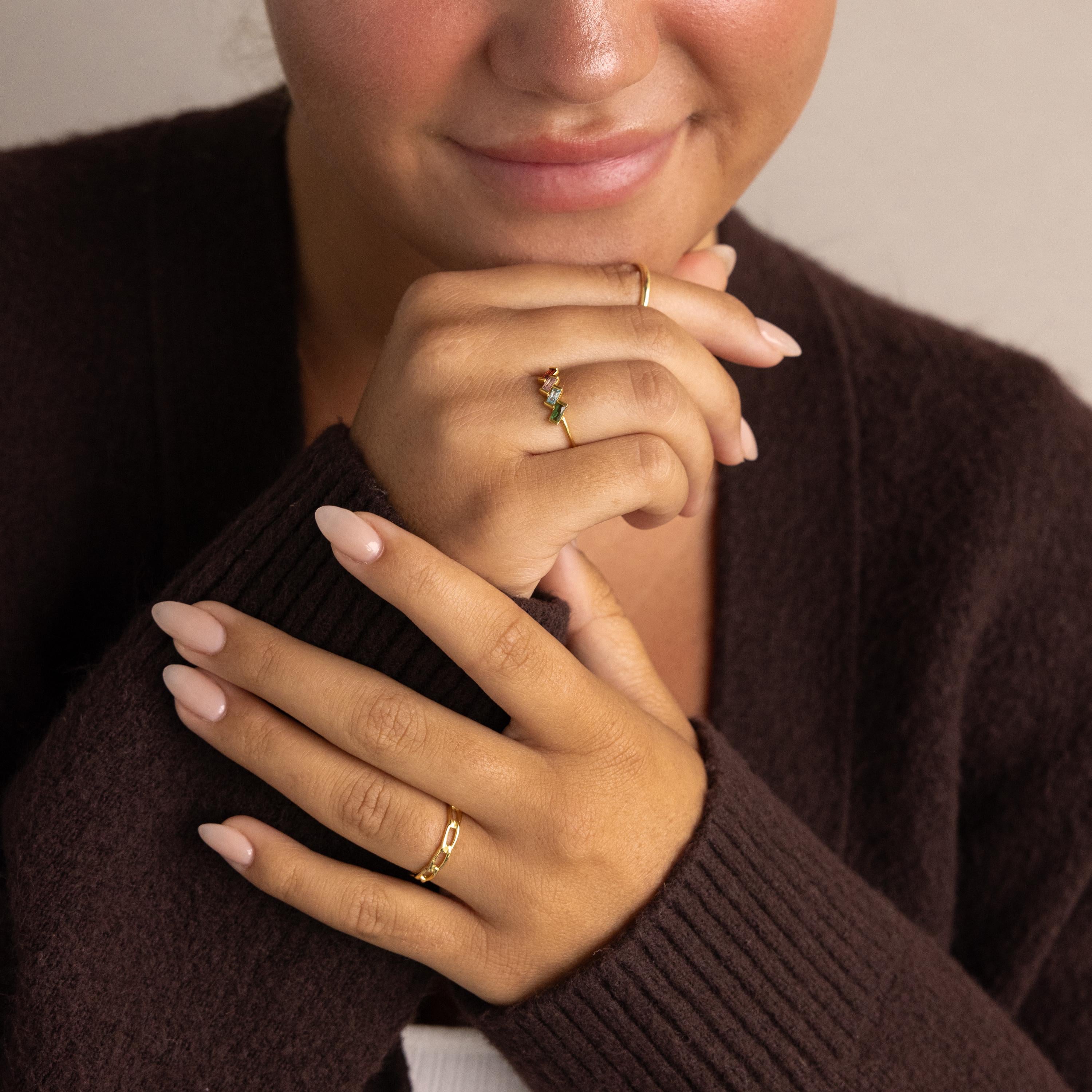 A woman with manicured nails wears the Multiple Baguette Birthstone Ring and a dark brown sweater, gently touching her face.