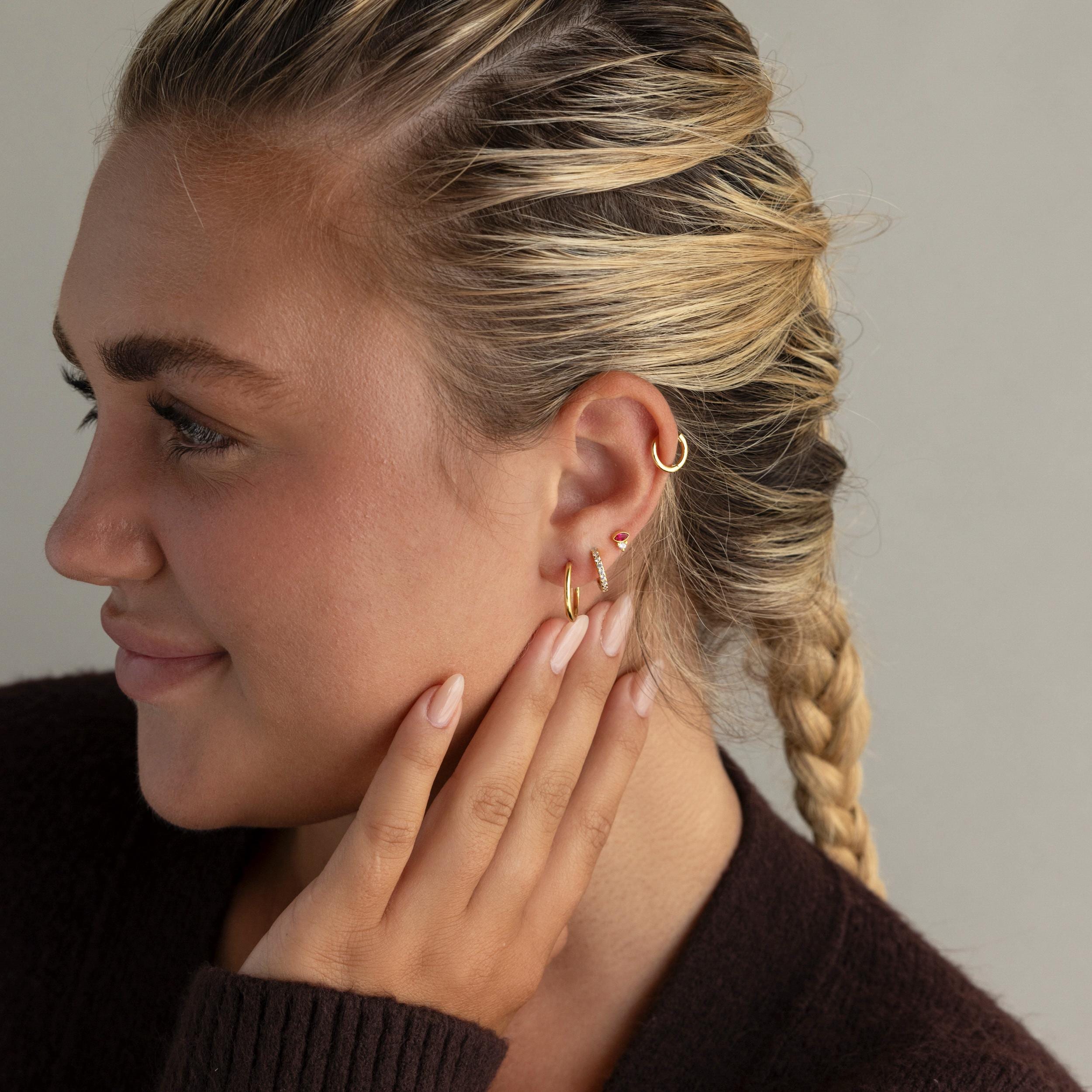 Woman with braided hair, wearing Diamond Marquise Birthstone Studs and a dark top, touches her ear while facing left.