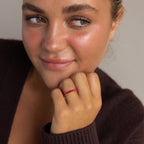 A woman with light eyes and rosy cheeks wears a dark sweater and the Eternity Marquise Birthstone Ring, smiling softly—the ideal Christmas gift.