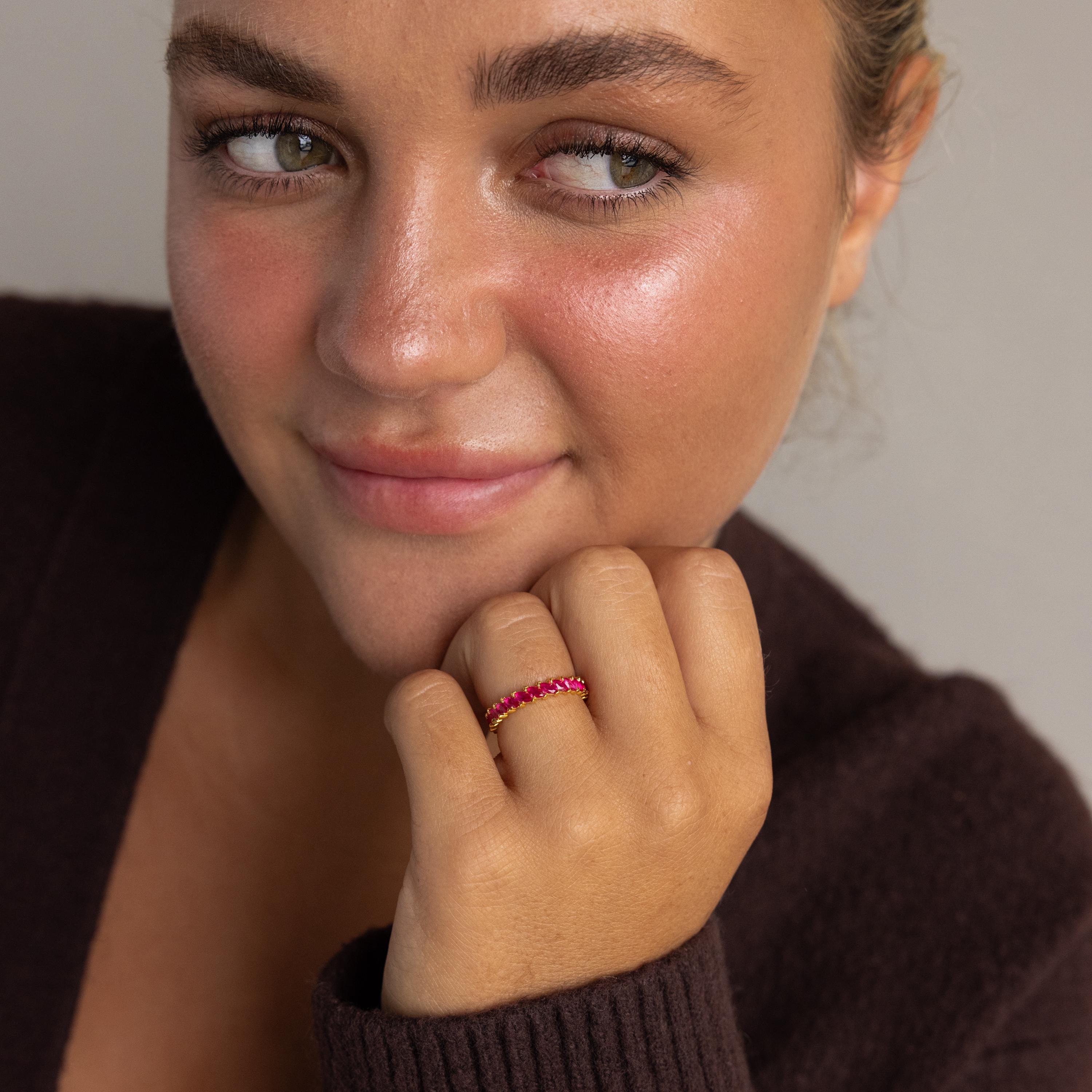 A woman with light eyes and rosy cheeks wears a dark sweater and the Eternity Marquise Birthstone Ring, smiling softly—the ideal Christmas gift.