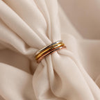 Three Engraved Tiny Name Rings in gold, silver, and rose gold rest on soft cream fabric—perfect minimalistic jewelry for a timeless look. Personalize each ring for a subtle, elegant touch to your style.