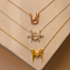 Three Modern Name Monogram Necklaces with unique metallic geometric pendants rest on a beige fabric background—ideal for those who love personalized jewelry and contemporary style.