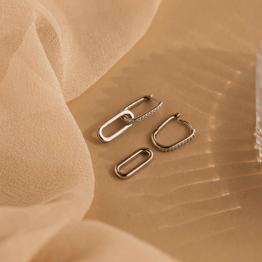 Pave Link Drop Earrings with sparkling CZ diamonds are showcased on a beige fabric backdrop, enhanced by soft lighting for a luxurious effect.