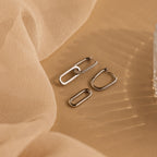 Pave Link Drop Earrings with sparkling CZ diamonds are showcased on a beige fabric backdrop, enhanced by soft lighting for a luxurious effect.