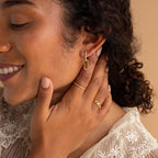 A woman smiles, wearing Pave Link Drop Earrings and rings, touching her face in a cream lace top against a beige background.