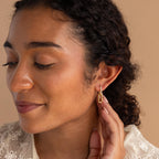 Woman with curly hair touches her Pave Link Drop Earrings, eyes closed, wearing a cream lace top against a beige background. Elegant CZ Diamonds accent these stylish earrings.