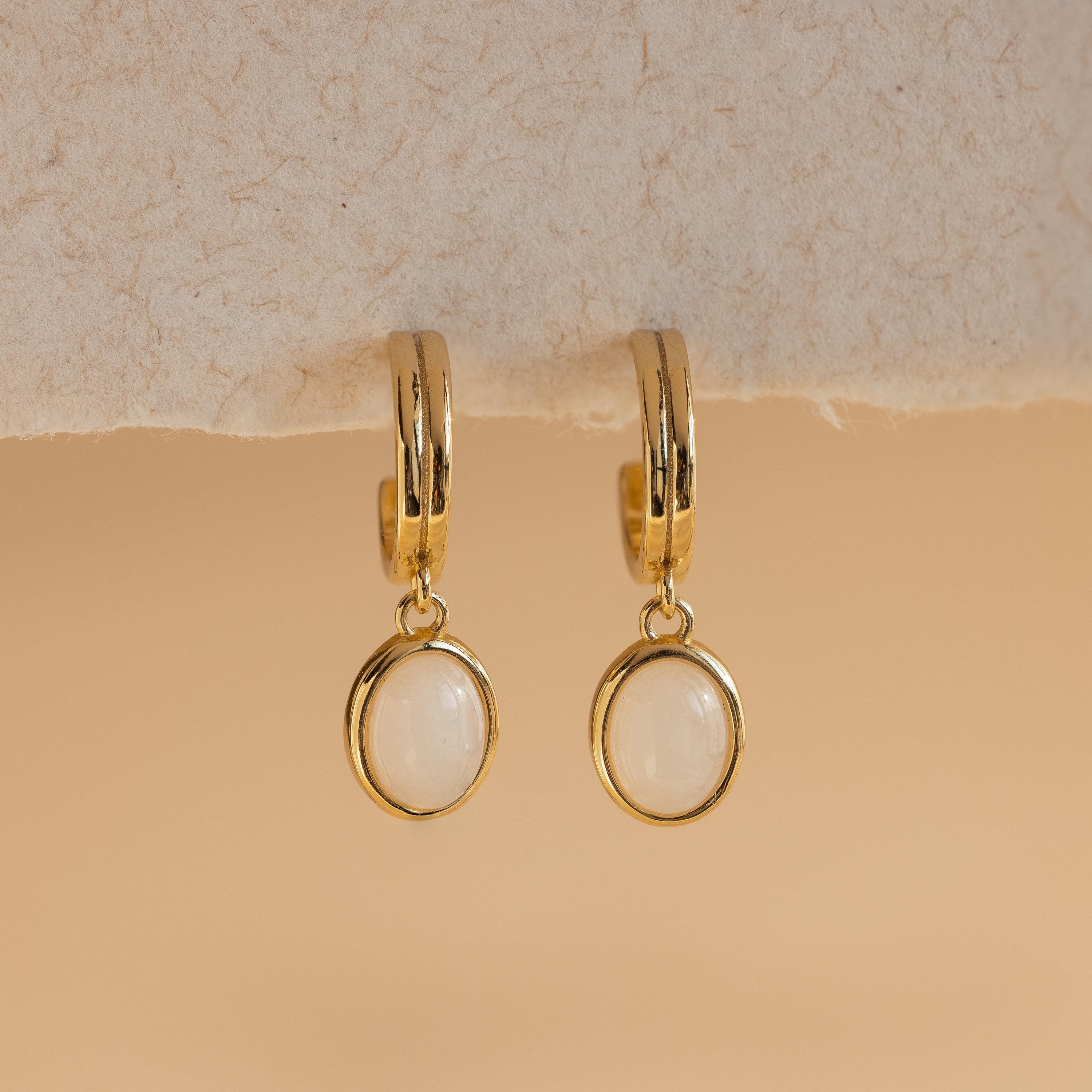 Moonstone Drop Hoops featuring oval white moonstones, elegantly suspended against a soft beige background—a refined celestial jewelry statement.
