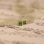 Delicate Ivy Flower Birthstone Studs, small green gemstone earrings, rest on sheet music with sheer fabric gently draped around them.