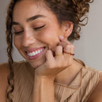 A smiling woman with curly hair rests her chin on her hand, wearing the customizable Engraved Birthstone Eternity Ring in gold and red.