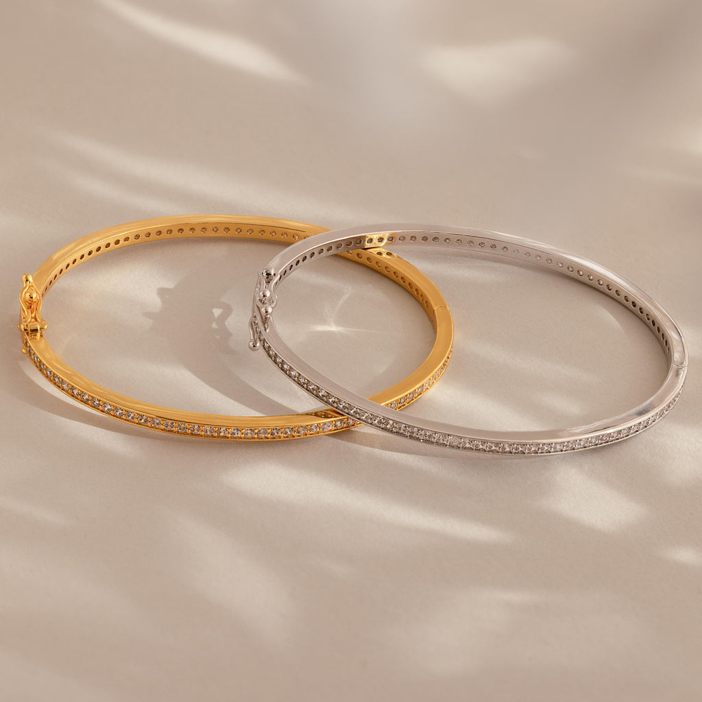 A Diamond Tennis Bangle with a sleek curved design rests on a beige surface, casting soft shadows.