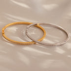 A Diamond Tennis Bangle with a sleek curved design rests on a beige surface, casting soft shadows.
